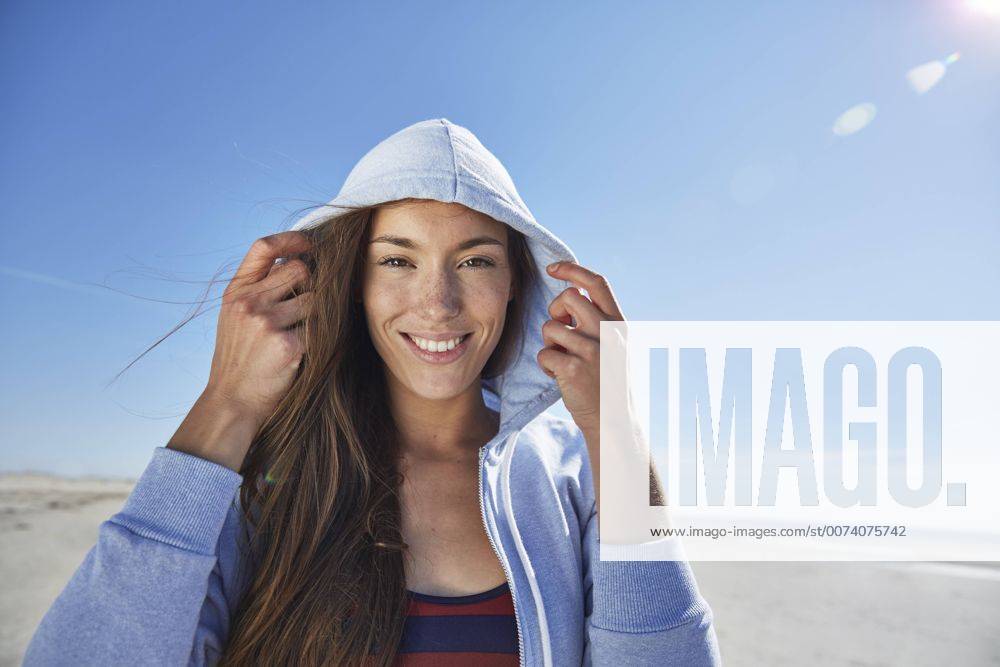 Youniverse - Young Holidays Smiling young woman wearing hoodie on the beach model released Symbolfoto SRYF000082