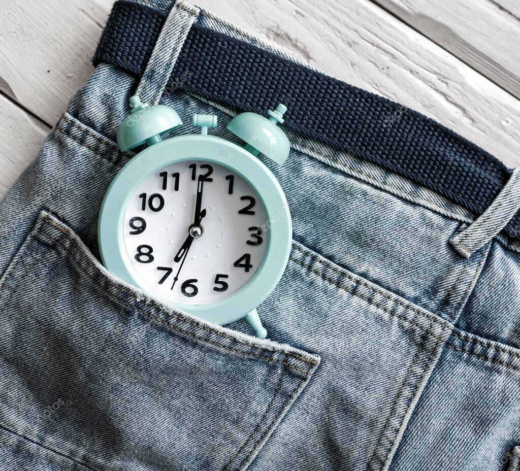 Top view retro alarm clock denim pants pocket. The concept of time on the clock hands 7 am.