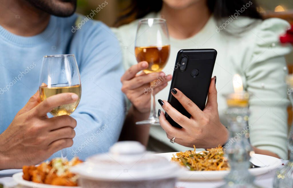Close up shot of couple hands using mobile phone by having drinks during candlelight dinner - concept of wedding anniversary celebration, cyberspace and dating application.