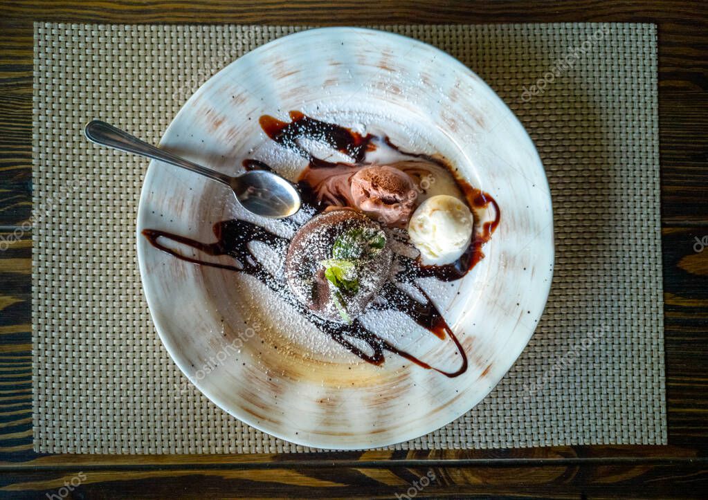 Photo of italian panna cotta dessert with strawberry sirup and mint leaf on the black wooden background. Ice cream. Metalic spoon.