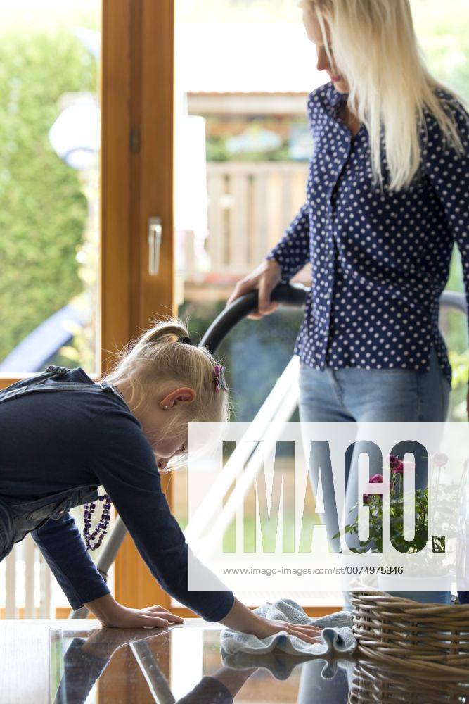 Girl cleaning glass table while her mother hoovering model released Symbolfoto property released MIDF00795