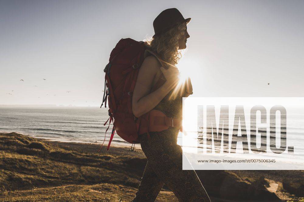 Youniverse - Young Holidays Blond teenage girl with backpack walking on the beach in the evening twilight model released Symbolfoto UUF08783