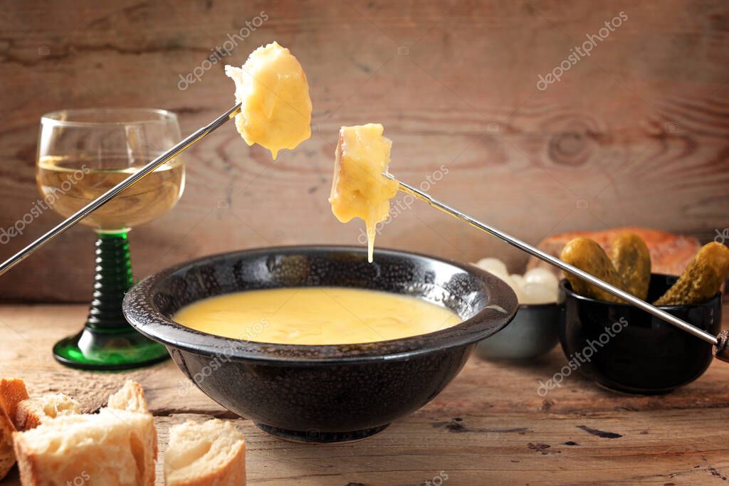 Swiss fondue from melted cheese with bread on long forks, pickles and wine on rustic wooden planks, copy space, selected focus, narrow depth of field