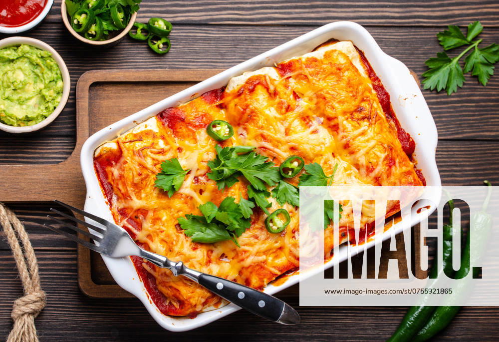 IMAGO Creative, Food, Enchiladas Traditionelles mexikanisches Gericht Enchiladas mit Fleisch, roter Chilisauce und Käse in einer weißen Auflaufform auf rustikalem Holzuntergrund, serviert mit Guacamole und Tomatendip. Nahaufnahme, Ansicht von oben Traditional Mexican dish enchiladas with meat, chili red sauce and cheese in white casserole dish over rustic wooden background, served with guacamole and tomato dips. Close up, top view