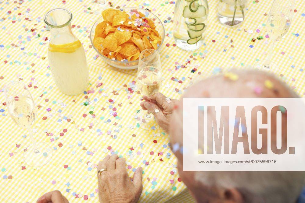Celebrating senior sitting at table with infused water, champagne and potato chips model released Symbolfoto property released MFRF00785