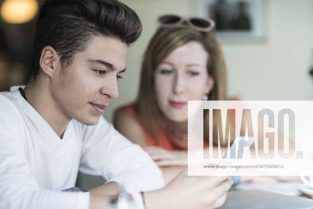 IMAGO Creative: Gesellschaft, Integration Teenage boy using cell phone with woman in background model released Symbolfoto TAMF00888