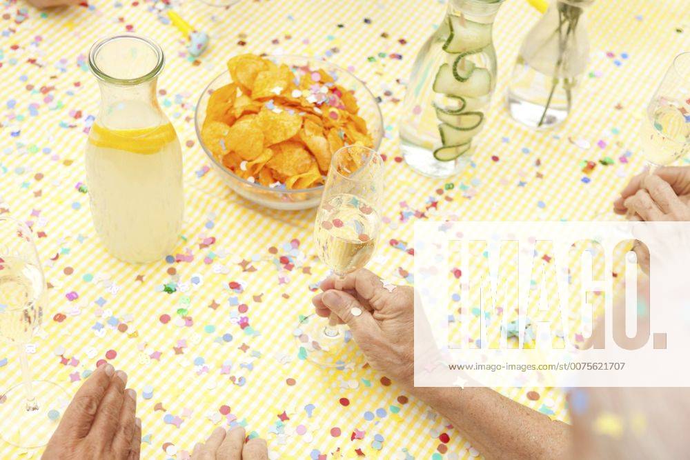 Celebrating senior sitting at table with infused water, champagne and potato chips model released Symbolfoto property released MFRF00784