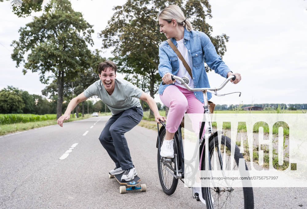 Cheerful man skateboarding with girlfriend riding bicycle on road model released, Symbolfoto, UUF32646