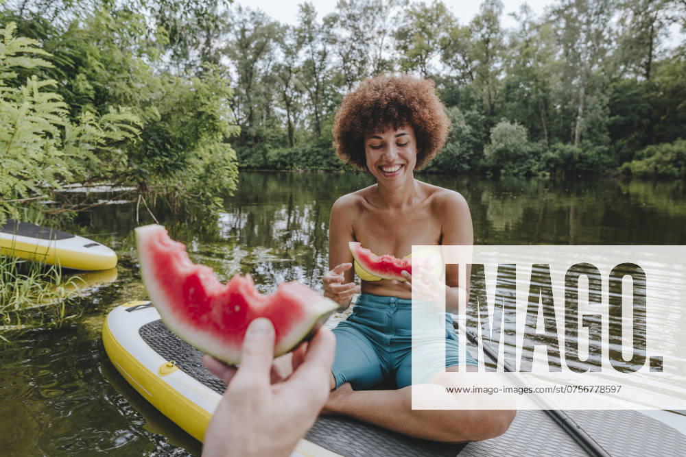 Happy woman eating watermelon with friend on paddleboard in lake model released, Symbolfoto, YTF01036