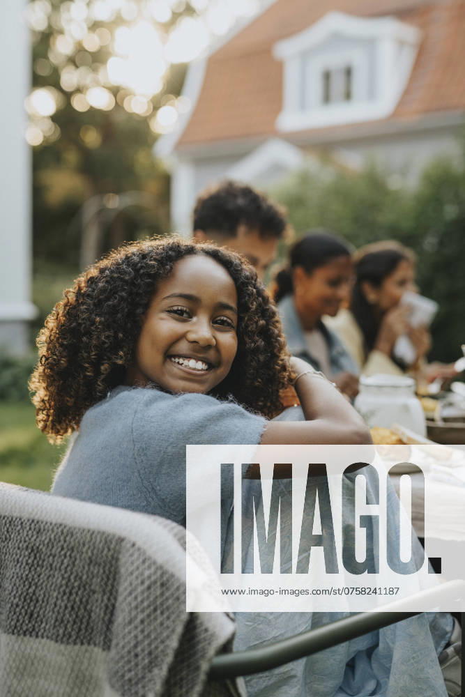 IMAGO Creative, Lifestyle, Feste im Garten #2 Portrait of happy curly hair girl sitting on chair at social gathering in back yard Sweden, Gothenburg, model released, property released