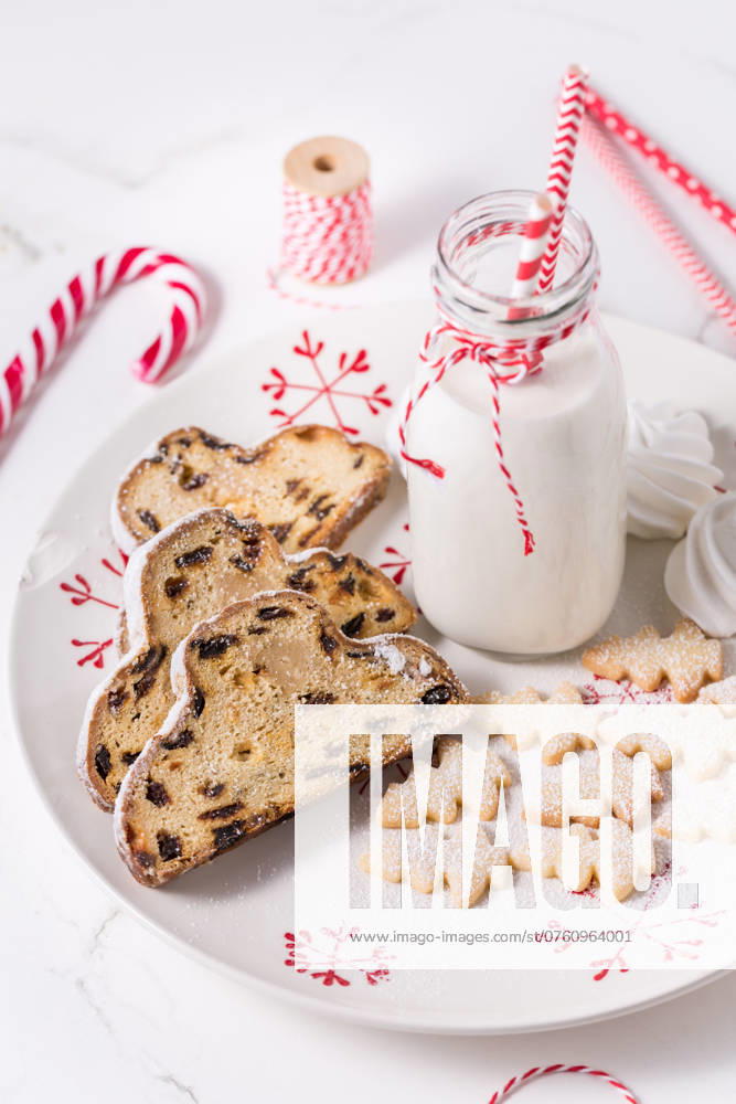 Flasche Milch mit traditionellem Christstollen, kleinen Keksen und Zuckerstangen auf weißem Hintergrund. Deutsches Weihnachtsbrot Bottle of milk with traditional Christmas stollen, small cookies and candy cane on white background. German Christmas bread