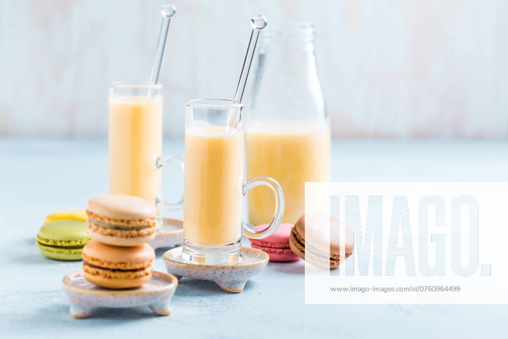 Verschiedene köstliche französische Macarons mit Eierlikör oder Eierlikör auf blauem Hintergrund Assorted delicious French macarons with egg liqueur or eggnog on blue background
