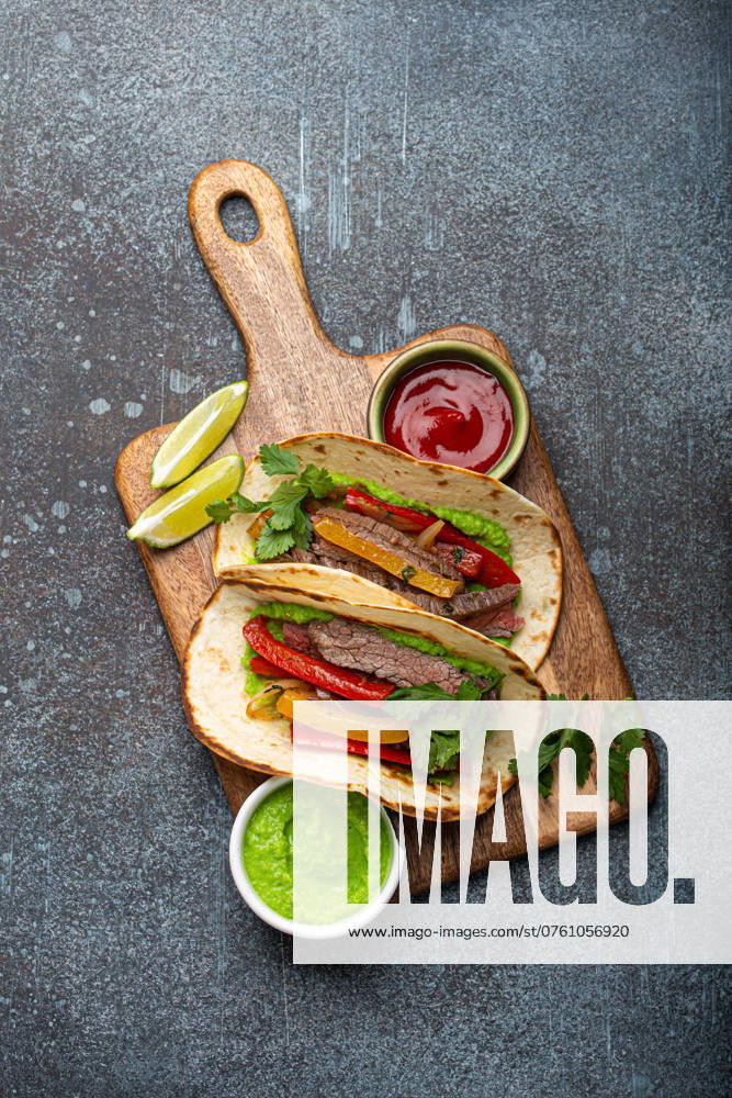 IMAGO Creative, Food, Fajita Traditionelles mexikanisches Gericht Rindfleisch Fajitas Tacos serviert auf hölzernen Schneidebrett mit Tomaten-Salsa und Guacamole auf rustikalen Stein Hintergrund von oben, American Mexican Food Traditional Mexican dish Beef fajitas tacos served on wooden cutting board with tomato salsa and guacamole on rustic stone background from above, American Mexican food