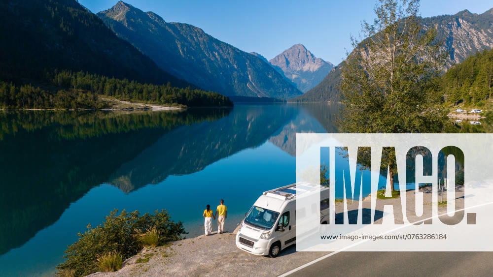 Exploring the tranquil shores of Plansee in Austria with a camper van at golden hour Two travelers enjoy the serene beauty of Plansee Austria, reflecting majestic mountains as their camper van rests nearby. The still waters and vibrant landscape create a peaceful getaway atmosphere. ,model released, Symbolfoto