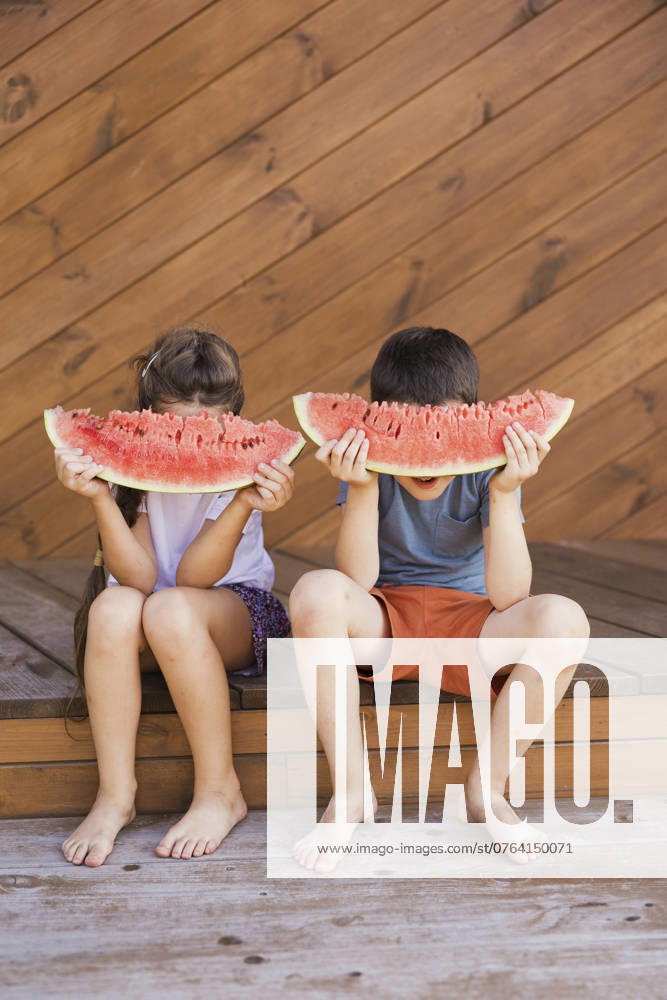 Boy and girl hiding faces with watermelon slices and sitting at porch model released, Symbolfoto, ONAF01016