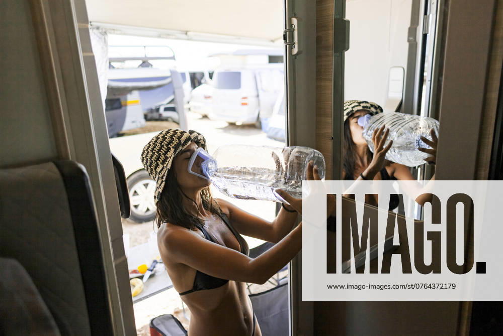 MR_ID23679_18259_ZaidaGimenezGayoso.jpg Side view of a young woman in a defined feminine style, at a music festival in the Monegros desert, refreshes herself by drinking water from a large bottle inside a camping van. The subject is looking down as she drinks. Model Released Almuzambrana_ID23679_687513_004