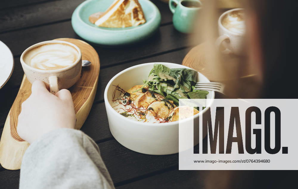 Cropped unrecognizable person enjoying a morning meal at a cafe, featuring a cup of coffee and a bowl with grilled halloumi and arugula, and a side of toast. Model Released HannaYakimenko_ID24020_696571_025