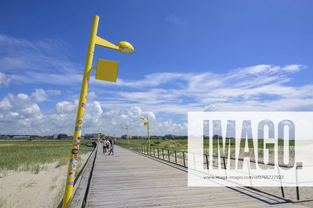Eine holzgeplankte Promenade führt entlang eines Strandes unter einem klaren blauen Himmel mit Wolken, Sankt Peter Ording, Schleswig Holstein, Deutschland, Europa A wooden-planked promenade leads along a beach under a clear blue sky with clouds, Sankt Peter Ording, Schleswig Holstein, Germany, Europe