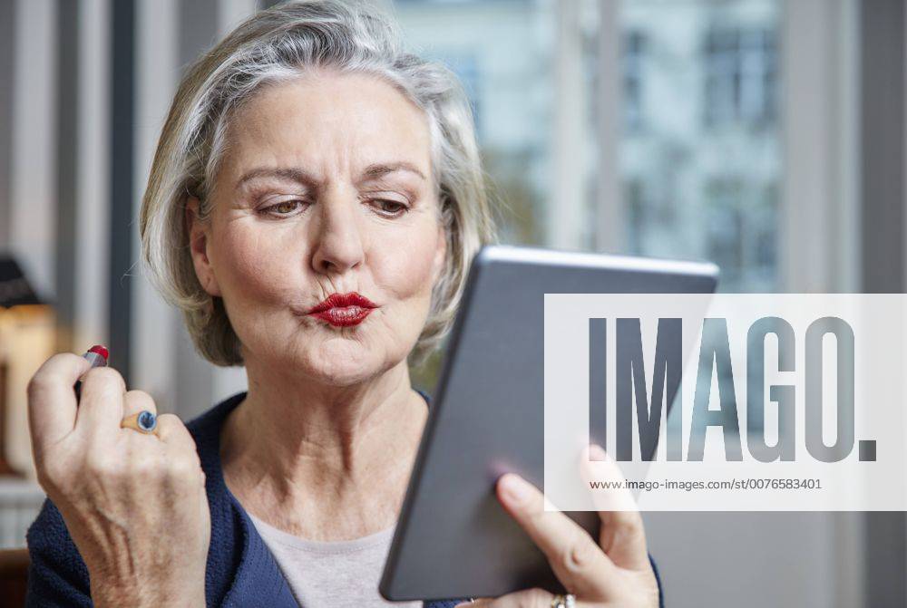 Senior woman applying lipstick holding tablet model released Symbolfoto property released RHF01794