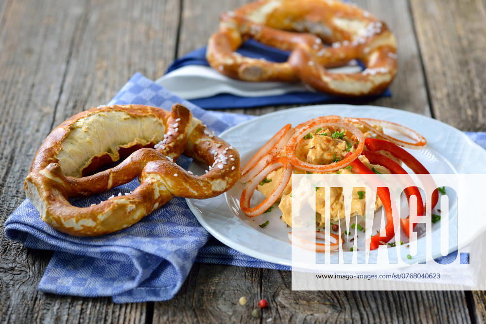 Portion Biergartenkaese Bayerische Käsespezialität - Portion Obazter mit Zwiebelringen und Brezel; A Bavarian snack: So called Obazda - cheese specialty made of melted camembert with cream cheese and butter, onions, a splash of beer and some spices - served with a pretzel on a white plate
