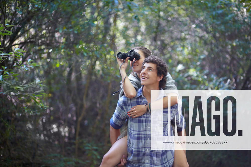 Man, woman and piggyback outdoor with binocular for travel, adventure or sightseeing in nature with happiness. Couple, people and tourist hiking in woods or forest for experience, holiday or vacation. model released property released