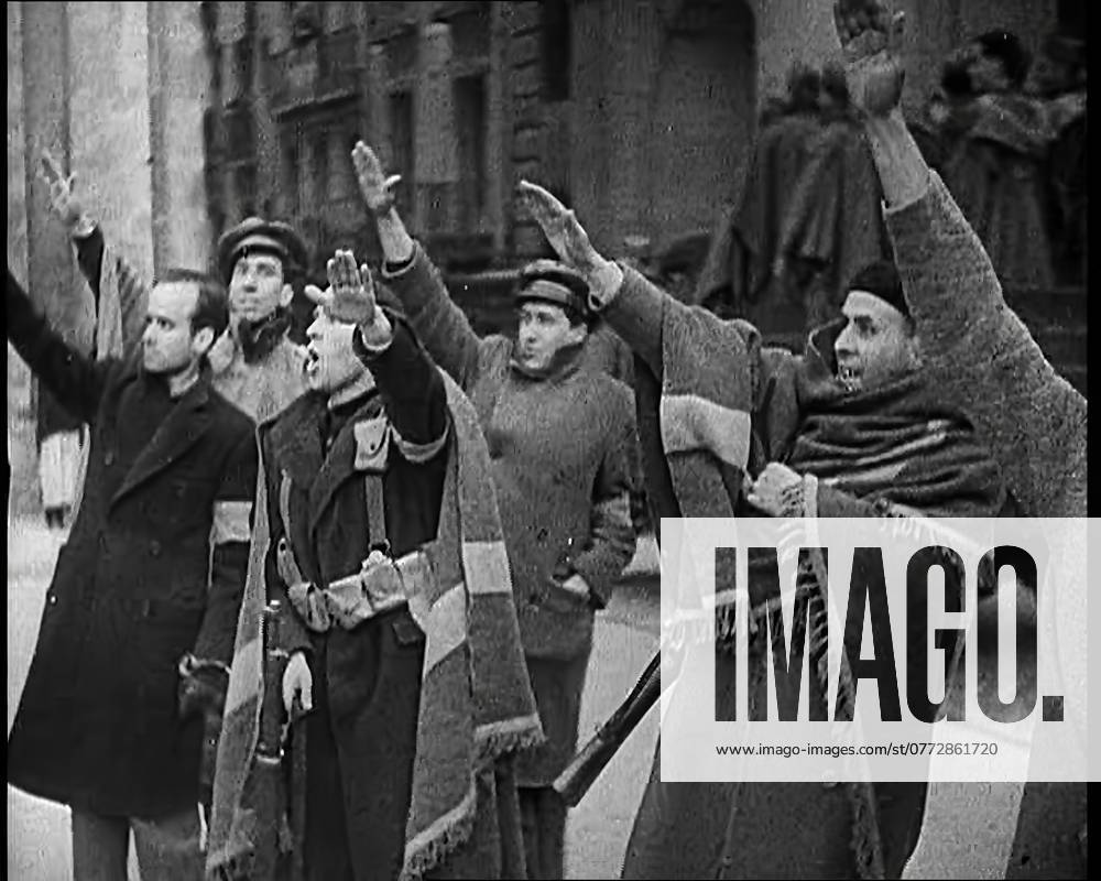 Armed Men and Civilians Making Fascist Salutes in a Street in Madrid, All Dressed in Thick Coats and Two With Blankets Draped Around Their Shoulders, 1939. From Time To Remember - The Reluctant Warriors, 1939 (Reel 1); documentary about events of 1939 - preparations for war and then hostilities break out.