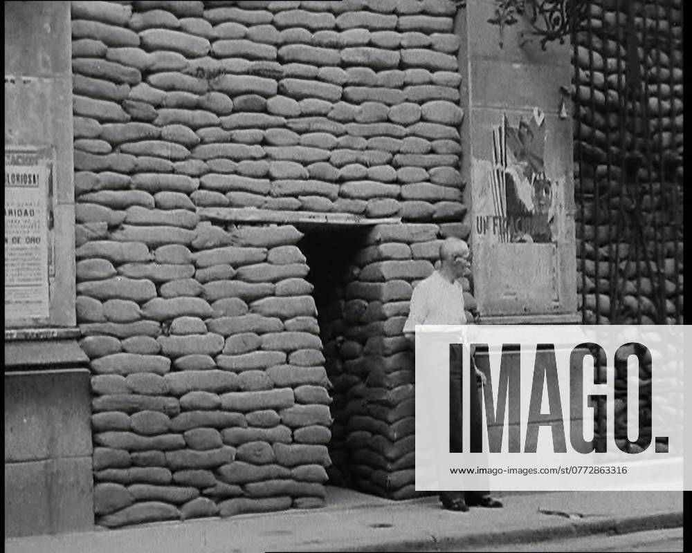 A Man Standing Outside the Frontage of a Building Obscured By Sandbags Next To an Ornamental Gate, 1937. Spanish Civil War. ...there was - alas - plenty of trouble...at large in Europe, particularly in places like Madrid. For the cities of Spain were the first to feel the breath of war in a truly modern manner. It has been said that war is but an extension of politics. True enough, particularly if it happens to be a civil war...Sandbags, air-raid shelters, the constant threat of sudden death . From Time To Remember - Sense Of Values, 1937 (Reel 2); documentary film about the events of 1937, war in the Far East, build up to war in Europe.