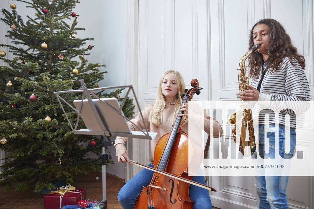 IMAGO Creative: Bildung, Musikerziehung Two girls playing cello and saxophone at Christmas tree model released Symbolfoto property released RHF01803