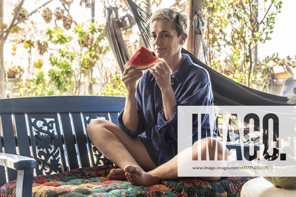 Thoughtful woman holding watermelon slice sitting cross-legged on bench model released, Symbolfoto property released, VGF00472