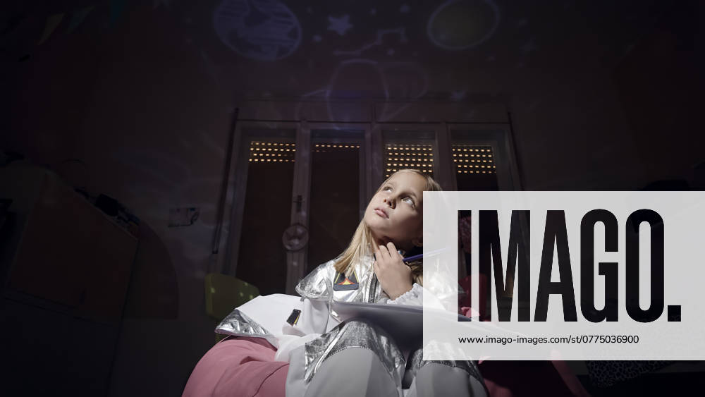 Thoughtful astronaut girl with paper fantasizing in dark bedroom at home model released, Symbolfoto property released, ZEDF04956