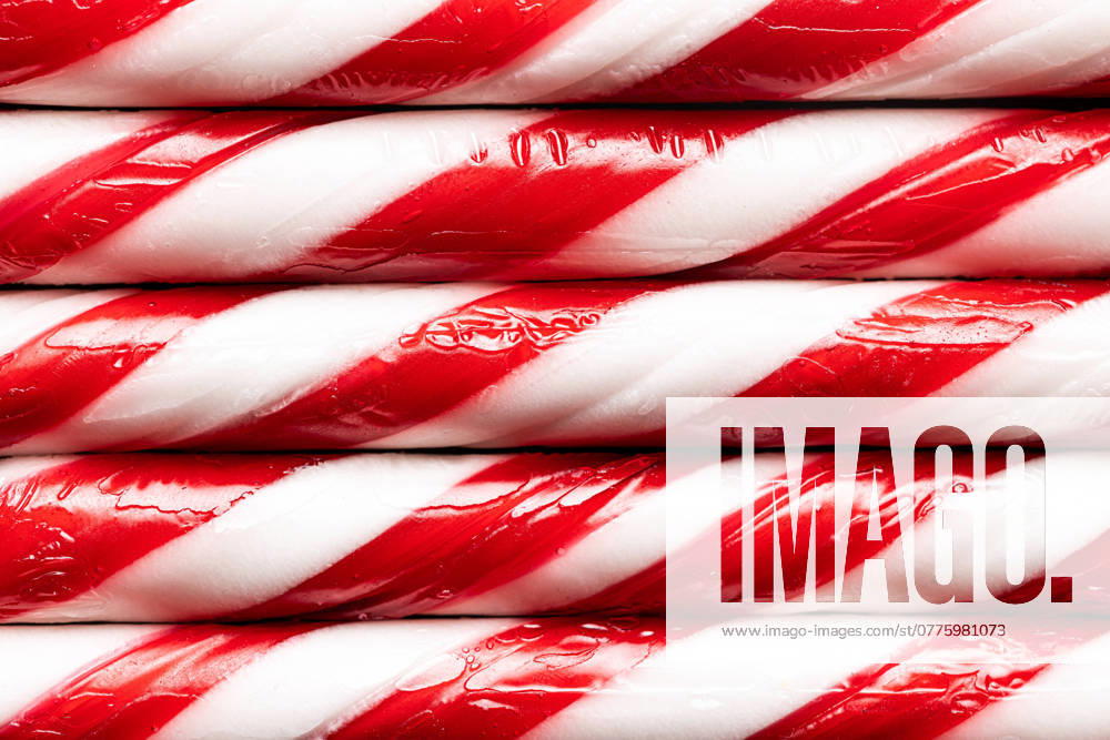 A close-up view of glossy red and white striped candy canes arranged tightly together, reflecting festive Christmas spirit. Model Released AlexSalcedo_ID24525_711110_027