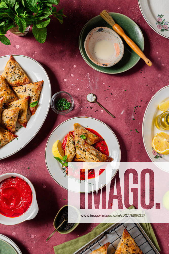 Delicious, crispy baked samosas on a red background, garnished with fresh mint and sesame seeds, accompanied by vibrant tomato sauce, portraying a vegan and healthy recipe ideal for Easter Model Released CintiaViudez_ID24446_708487_005