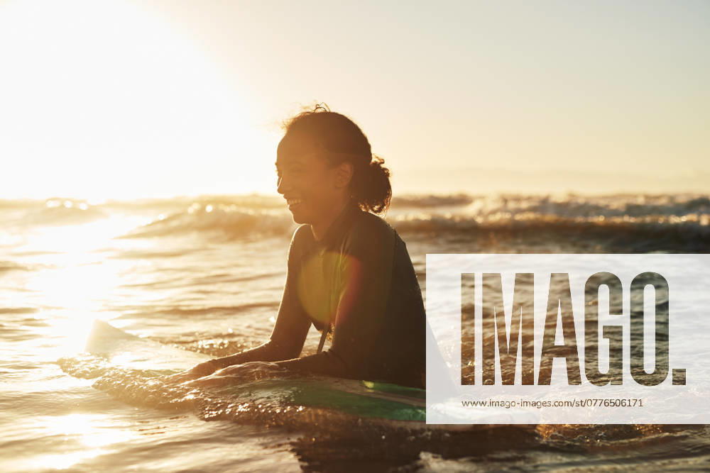 Surfer, woman and swimming in ocean with wetsuit for summer adventure, sunset and fun activity in water. Girl, surfing sport and floating in waves with board for vacation travel, exercise and peace. model released property released