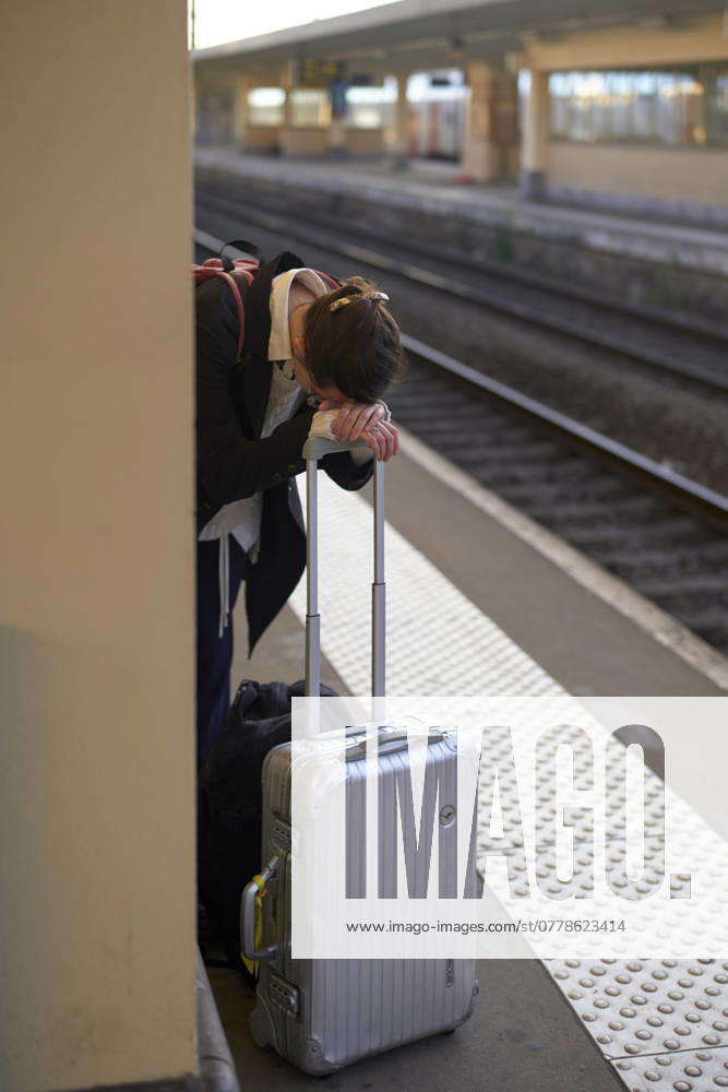 IMAGO Creative, Gesellschaft, Leisure Sickness Exhausted traveler resting on a suitcase at a train station platform. bola04432