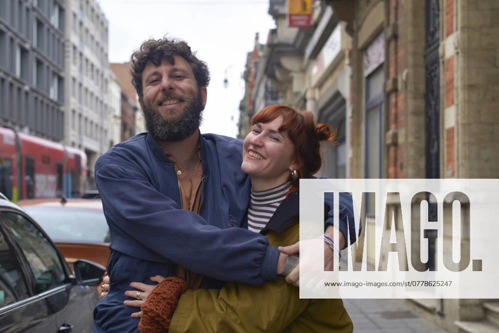 Smiling bearded man giving piggyback ride to a cheerful redhead woman on a city street, Brussels, Belgium bola04698