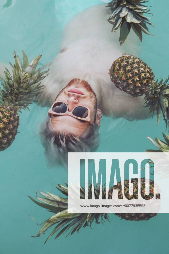 Young man in swiming pool surrounded by pineapples model released Symbolfoto RTBF00748