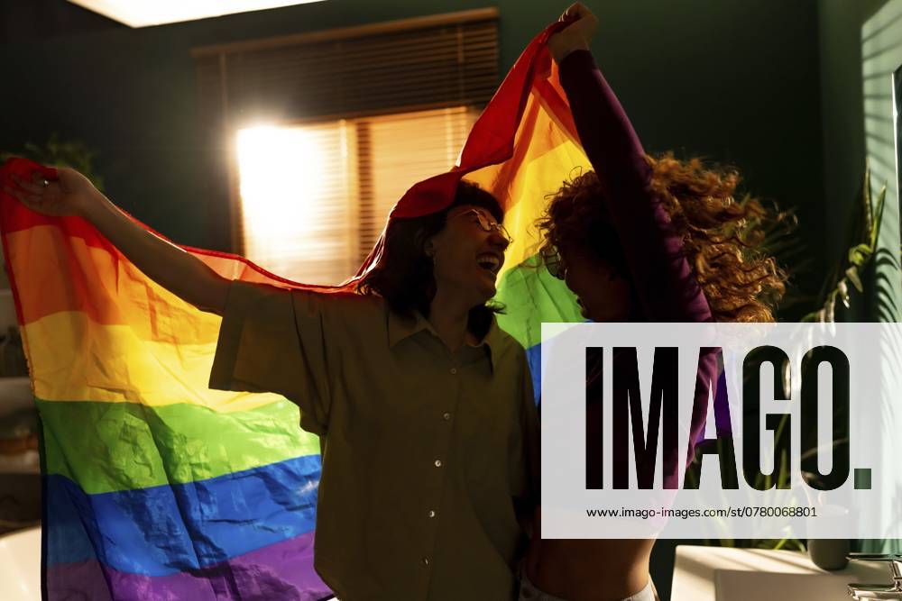 Romantische glückliche lesbische Paar tanzen und winken Regenbogen lgbt Flagge drinnen Romantic happy lesbian couple dancing and waving rainbow lgbt flag indoors