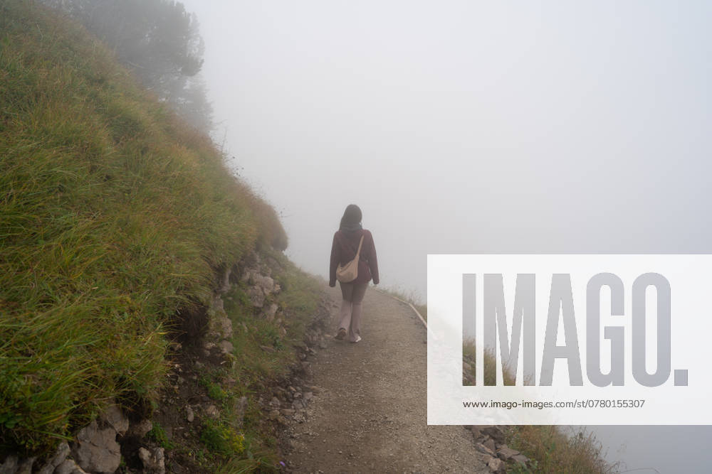 A solitary hiker traverses a foggy mountain path in Stoos, Switzerland, creating a scene of serene isolation amidst the enveloping mist Model Released JuanAlbertoRuiz_ID24623_713579_006
