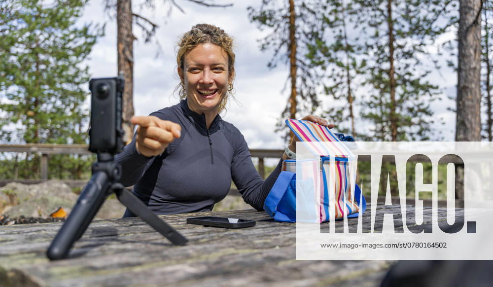A joyful woman relishes her lunch outdoors while trekking in the serene Muddus National Park, located in Lapland, Sweden She is capturing the moment using a camera on a tripod Model Released VictorCuenca_ID24674_714855_004