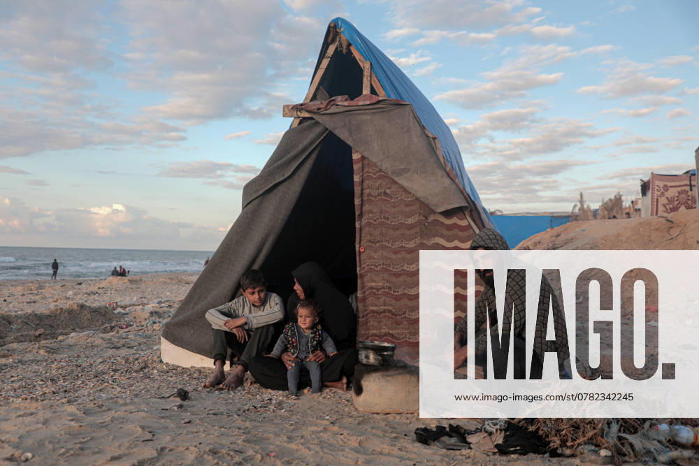 (241129) -- GAZA, Nov. 29, 2024 -- Odai Olaiwa (1st R) and his family are pictured beside a tent on the seaside in the city of Deir al-Balah in central Gaza Strip, Nov. 28, 2024. Odai Olaiwa, a 35-year-old father of three children, was forced to flee from Gaza City with his family at the onset of the Gaza conflict. They transferred to the city of Deir al-Balah in the central Gaza Strip six months ago, huddling inside a tent on the seaside that could barely shield them from the scorch in summer or the frost in winter. Three days earlier, seawater flooded his tent and soaked his belongings. The tent was then destroyed by heavy winds, and the Olaiwa s became homeless again. They had to stay in their relatives tent and live on food offere