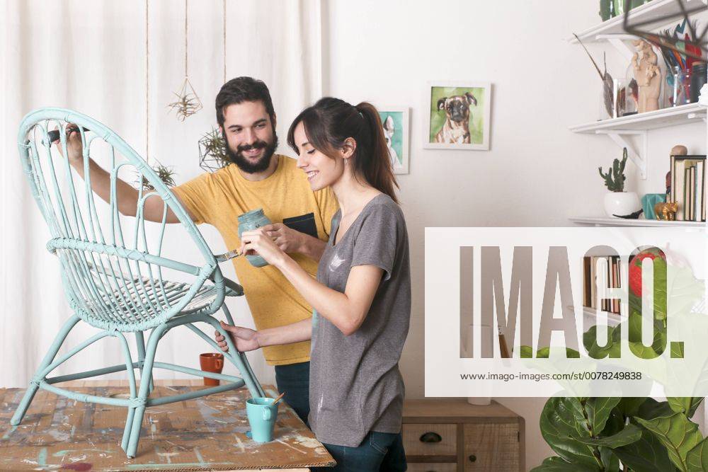 Young couple painting wicker armchair in blue at home model released Symbolfoto property released RTBF00777