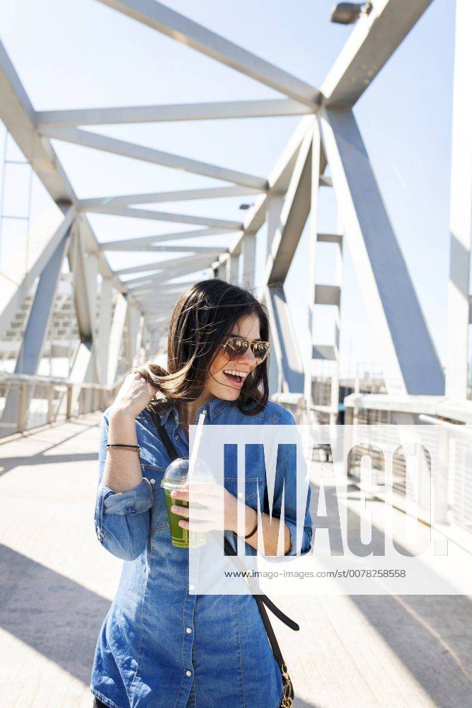 Spain, Barcelona, laughing young woman with beverage on a bridge model released Symbolfoto VABF01274