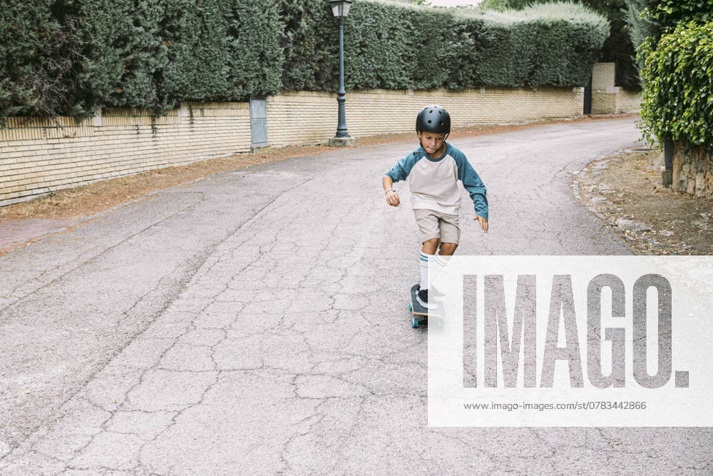 A young boy wearing a helmet rides a skateboard down a quiet suburban street The image captures the essence of childhood adventure and outdoor fun Model Released DavidBenito_ID25114_727152_016