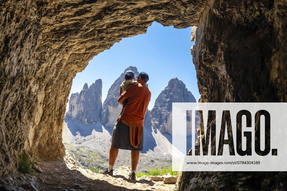 Vater hält seinen Sohn und bewundert bei einer Sommerwanderung die Dolomiten, die Tre Cime di Lavaredo, von einer Tre Cime Höhle aus Father holding his son admiring the tre cime di lavaredo, dolomites, from a Tre Cime Cave during a summer hike