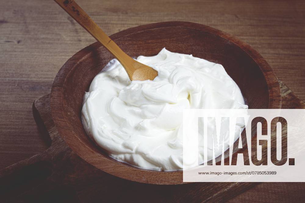 Saure Sahne in einer Holzschale, auf einem Holztisch, Draufsicht, Nahaufnahme, keine Personen Sour cream in a wooden bowl, on a wooden table, top view, close-up, no people