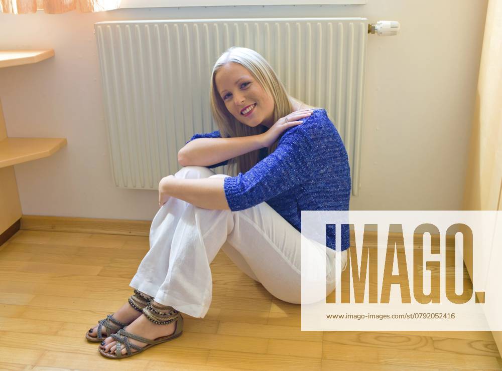 Eine junge Frau sitzt im Winter vor einem Heizkörper. Austria A young woman sits in front of a radiator in winter. Austria