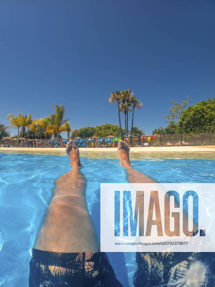 Beine eines Touristen, der in einem Schwimmbad in einem Wasserpark im Sommerurlaub schwimmt und entspannt Legs of a tourist floating and relaxing in a swimming pool at a water park during summer vacation
