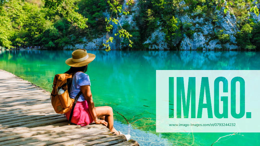 Ein ruhiger Moment am türkisfarbenen Wasser der Plitvicer Seen in Kroatien an einem sonnigen Tag Nestled amid lush greenery, a female traveler enjoys a serene afternoon at Plitvice Lakes Croatia, captivated by the vibrant turquoise water and the natural beauty surrounding the wooden walkways. ,model released, Symbolfoto