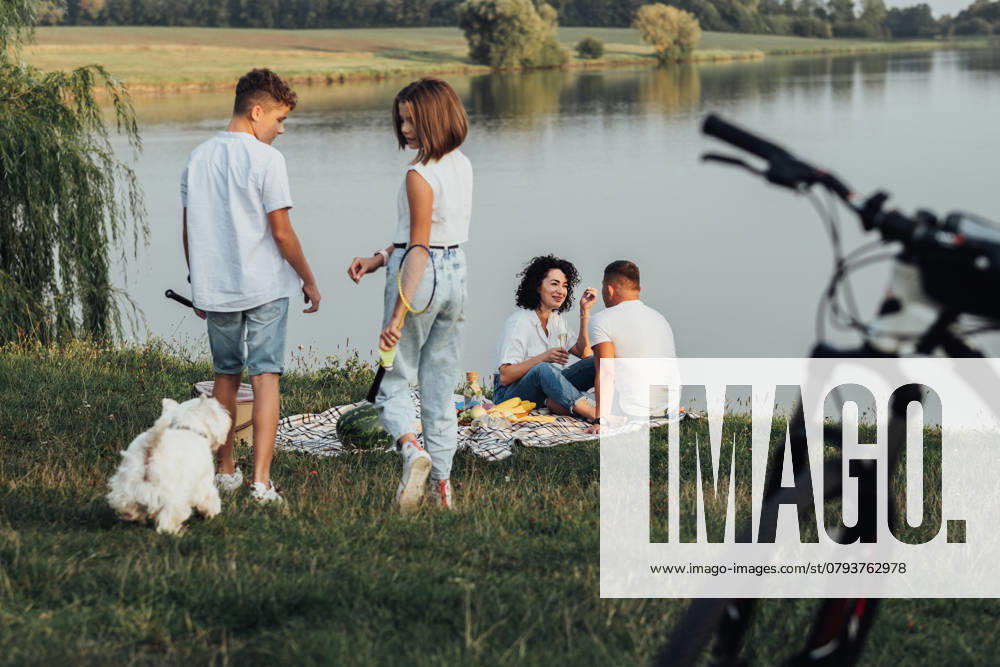 Middle Aged Man and Woman Having Picnic While Their Two Teenage Children, Son and Daughter Playing with Pet Dog, Happy Four Members Family Enjoying Weekend Outdoors by Lake, model released, , 47286172.jpg, family, four members, mother, father, woman, man, middle aged, children, teenage, daughter, son, kids, happy, parents, childhood, parenthood, together, girl, boy, female, male, pet, dog, west highland white terrier, lake, river, water, bicycle, picnic, outdoors RECORD DATE NOT STATED