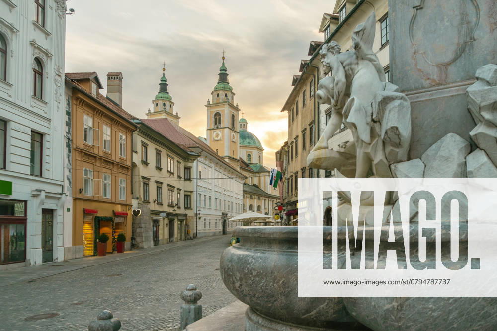 Sunset illuminates an old European street Sunset illuminates an old European street with a foreground focus on a stone fountain and historic St. Nicholas Church in the background, Ljubljana, Slovenia Ljubliana Slovenia taar04595